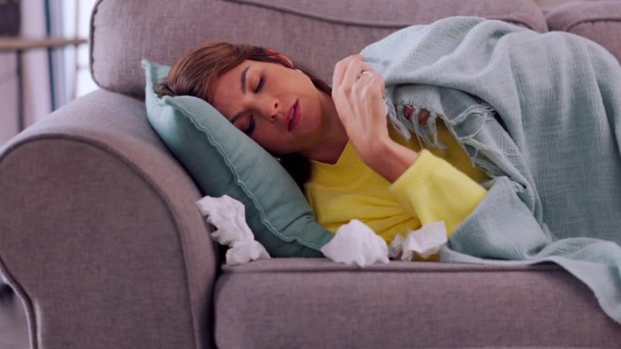 生病，感冒，一个女人在沙发上擤鼻涕，同时患有流感，鼻窦或过敏。Covid，咳嗽和疲倦的女孩躺在沙发上