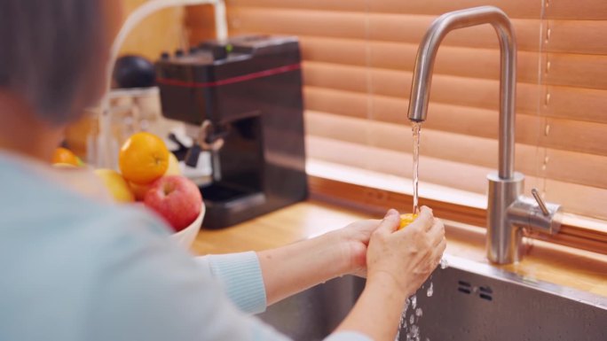 近距离观察老年妇女家庭主妇在家中厨房洗橙手。有吸引力的成熟管家清洁和清洗健康的水果和蔬菜用清水准备早