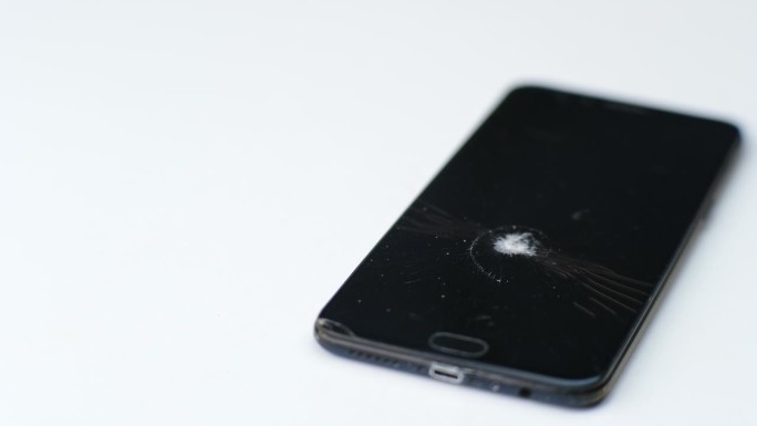 破碎的黑色触屏手机孤立在白色背景上。因撞击或锤击而有裂缝的碎玻璃。智能手机损坏，触摸屏被蜘蛛网划伤。
