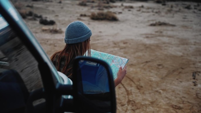 在沙漠的某个地方，一名妇女看着她的露营车前的地图