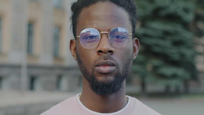 非裔美国学生戴眼镜站在户外，表情严肃的慢动作肖像