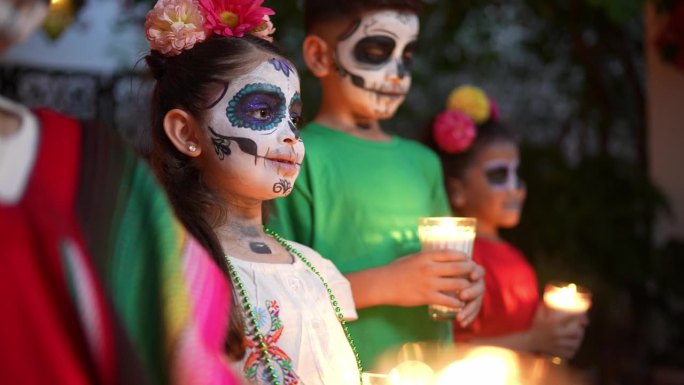 孩子们脸上画着糖骷髅，手持蜡烛庆祝亡灵