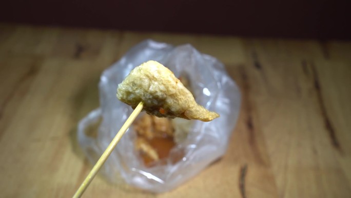包在塑料袋里的油炸肉丸，上面淋上美味的蘸酱。准备吃饭时用木棒把木棒放在木桌上。