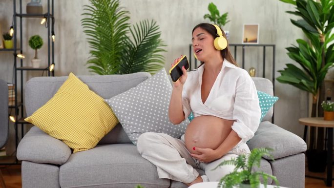 年轻的孕妇在客厅里听音乐