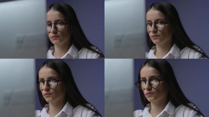 戴着眼镜的年轻女性在办公室用笔记本电脑工作。一个人专注于工作。镜头移动缓慢，流畅，像电影一样。眼镜显
