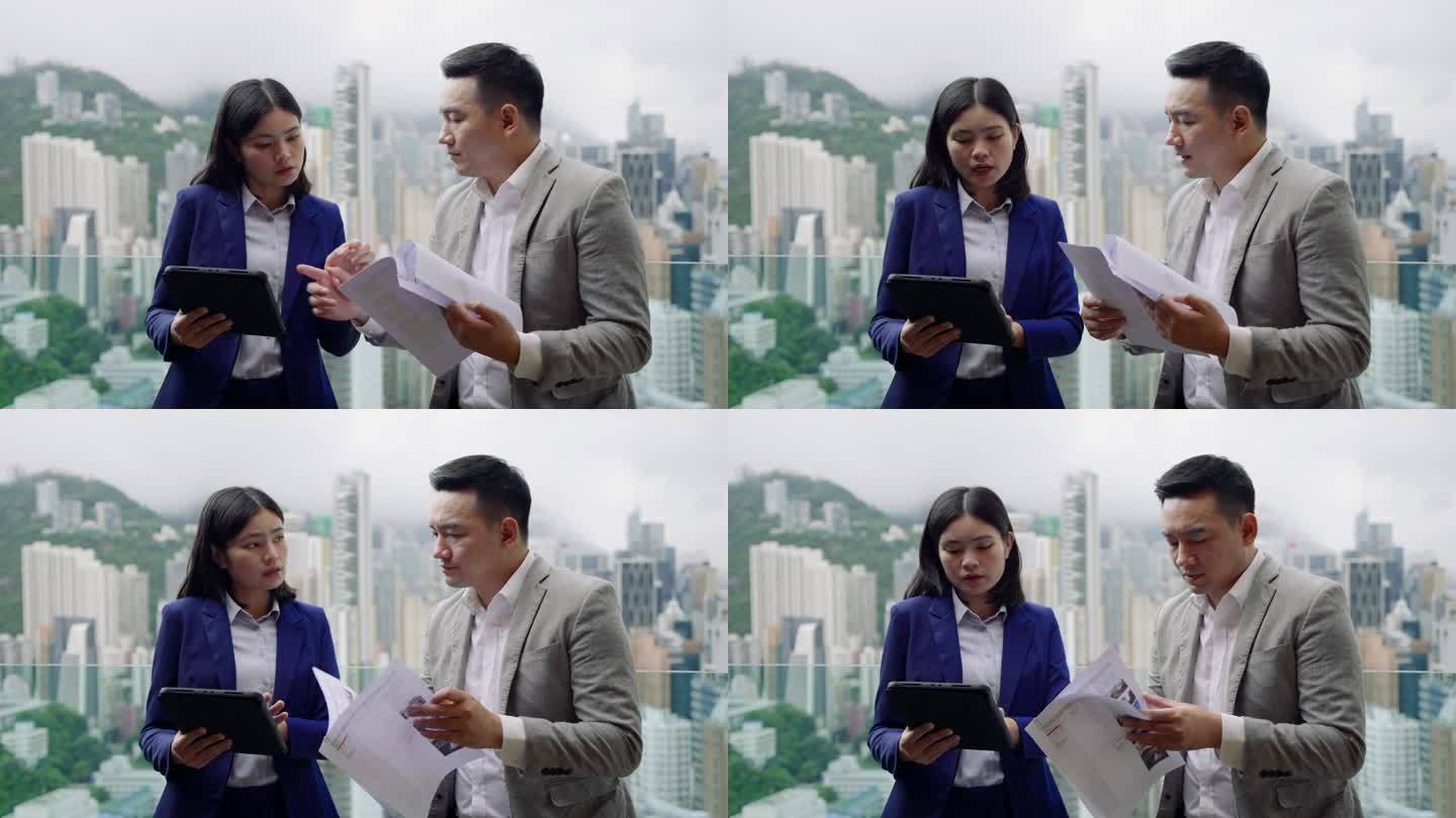 商业伙伴在窗边讨论工作，背景是香港岛的建筑景观。