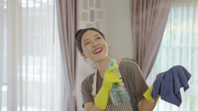 快乐的年轻主妇小三女戴着黄色防护橡胶手套，带着喷雾和抹布，打扫屋子，享受家务，亚洲女佣致力于保持最高