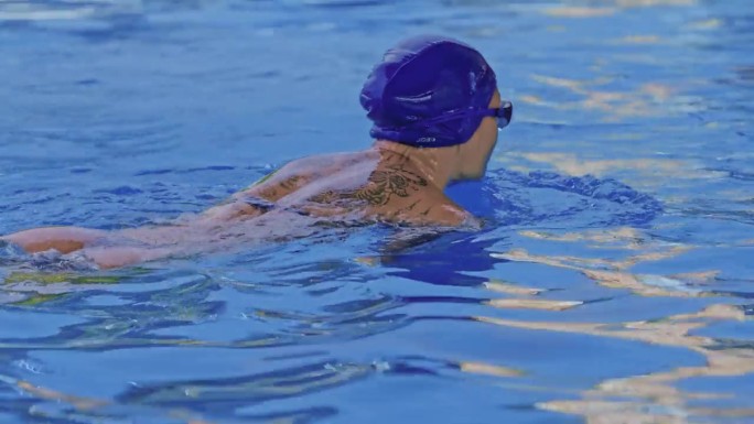 一名职业女游泳运动员在泳池边戴着护目镜的侧视图。一位女游泳者跳入水池。特写，慢镜头。