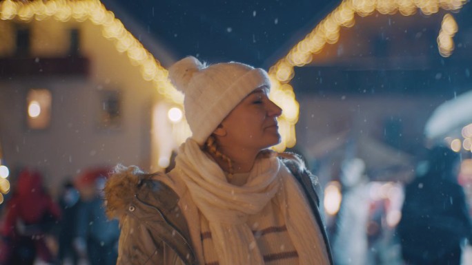 一位女士在雪地里欣赏圣诞市场上的装饰品和彩灯