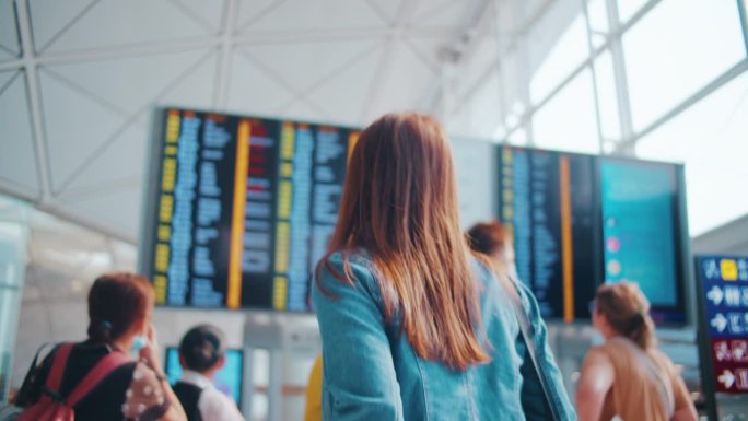 女旅客在离境板前，旅客在机场查看航班信息显示屏