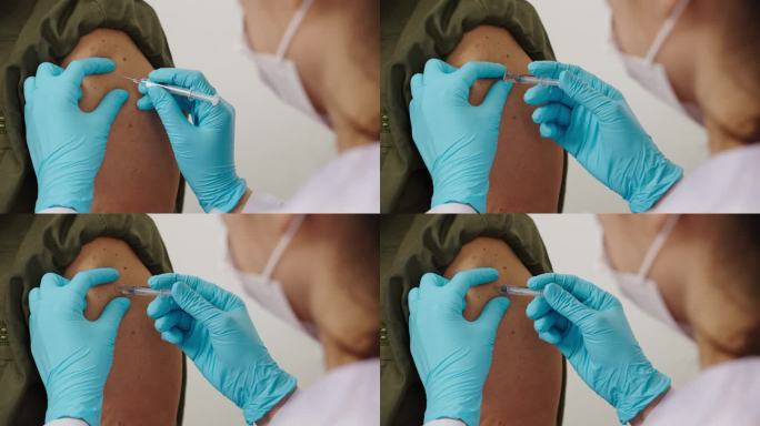 医生戴着手套，拿着注射器，给戴着医用口罩的病人注射。Covid-19或冠状病毒疫苗