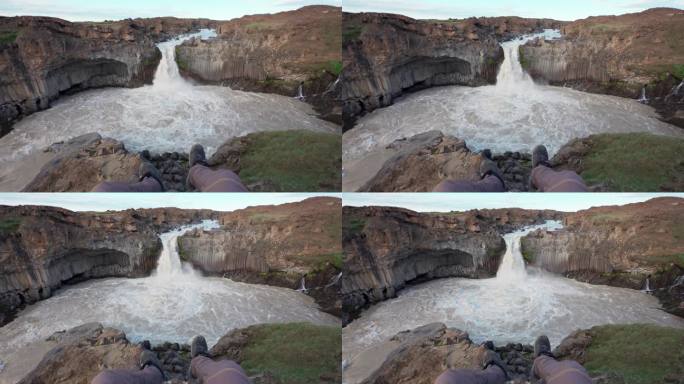 冰岛夏季，男性旅行者坐在强大的阿尔德雅福斯瀑布悬崖上，瀑布从熔岩场和玄武岩柱中流出