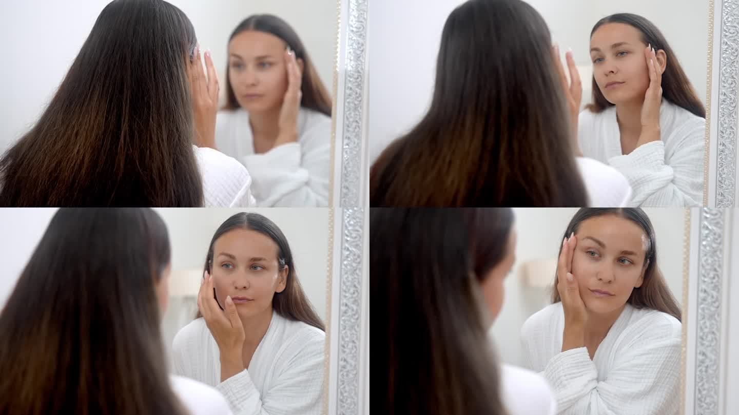 一名穿着浴袍的女子，在浴室的镜子前审视着自己，沉浸在美容护肤的概念中。