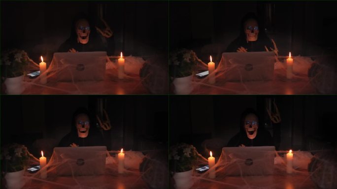 令人毛骨悚然的死亡人物，手提电脑旁边的黑屋子里的骷髅和蜘蛛网里的蜡烛。