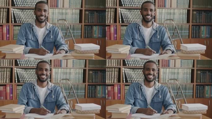 欢快的非裔美国学生的慢动作肖像，坐在图书馆的桌子上，拿着书、笔记本和笔