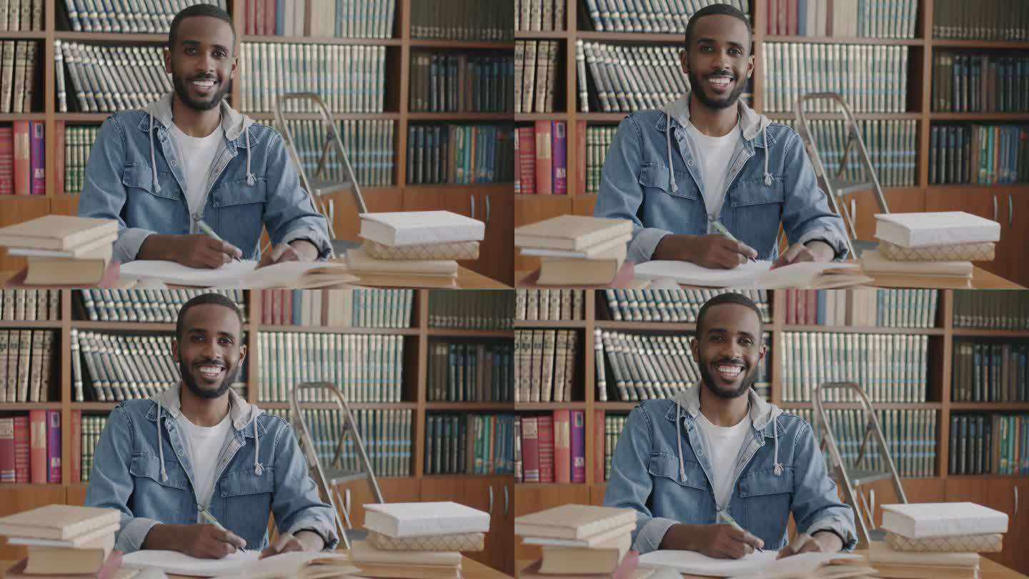 欢快的非裔美国学生的慢动作肖像，坐在图书馆的桌子上，拿着书、笔记本和笔