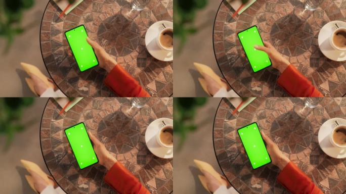 顶部静态视图的女性业务经理滚动通过智能手机上的应用程序与绿屏Chromakey模拟显示在户外咖啡馆。