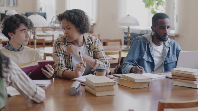 快乐的年轻人，大学生，写作，阅读，一起学习，然后坐在图书馆的桌子上聊天