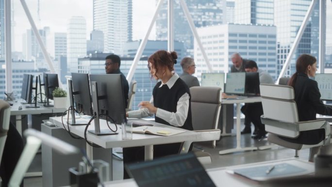 年轻的女性数据科学家在明亮和多样化的公司办公室的台式电脑上打字，拥有大都市的窗口视图。与同事一起在科