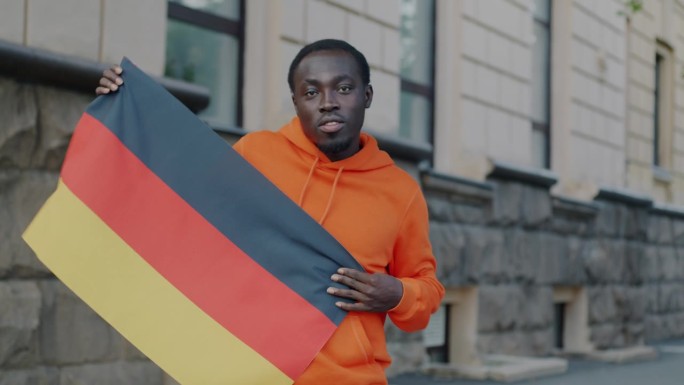 一个无忧无虑的非洲裔美国人拿着德国国旗跳舞，微笑着看着镜头的慢动作肖像