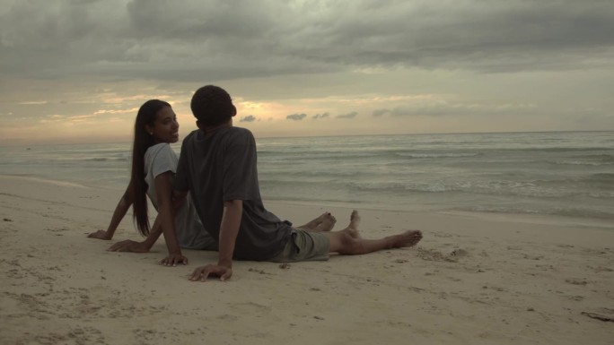 年轻夫妇坐在海边聊天，望着别处