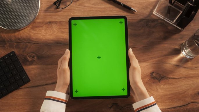 一个匿名的创意年轻人持有平板电脑与模拟绿屏Chromakey显示器垂直俯视视图。设计师查看在线演示文