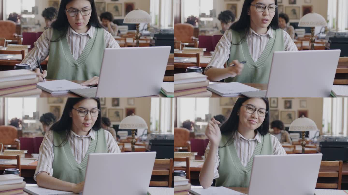 开朗的亚洲女学生在大学图书馆用笔记本电脑打字、浏览、记笔记和写笔记