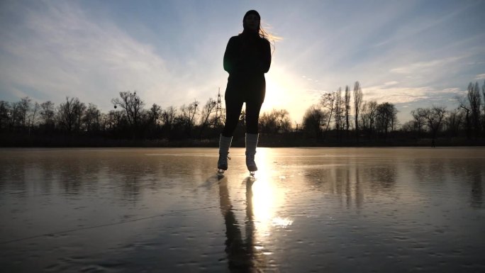穿着溜冰鞋的年轻女子在结冰的湖面上滑行。女孩正在滑冰，背景是美丽的阳光。冬日河上的夕阳。冬季积极生活