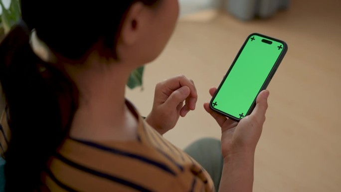 拿着绿屏智能手机的女人坐在家里的地板上。