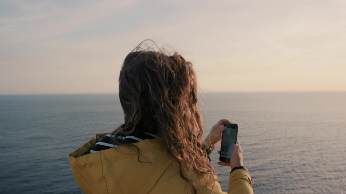 女子用智能手机拍摄日落，女孩用柔和的光线拍摄日出海景，享受假期旅行冒险