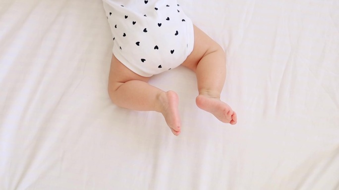 一个小孩的腿躺在浅色的床上或白色的背景上，一个书写文字的地方，一个婴儿的脚
