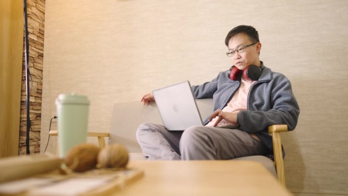 远程工作，男人在家里用笔记本电脑在客厅的沙发上工作