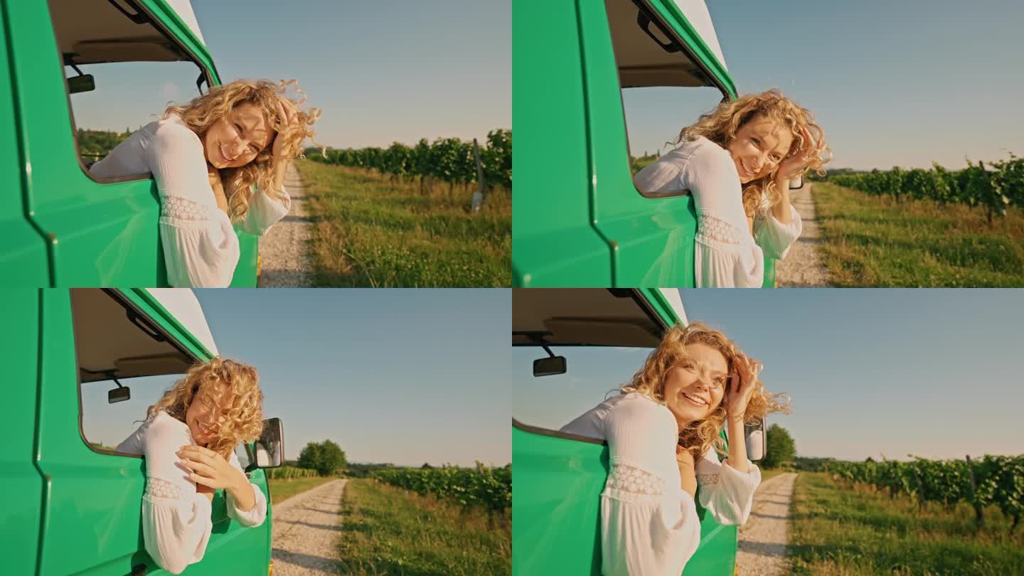快乐的金发女子探出汽车之家的车窗，拥抱着风景秀丽的乡村道路