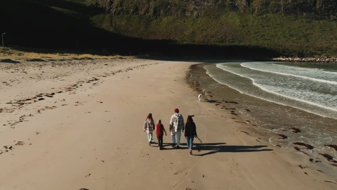 一架无人机在挪威厄斯峡湾海滩拍摄了一个带着两个孩子和一只狗在海边散步的年轻家庭