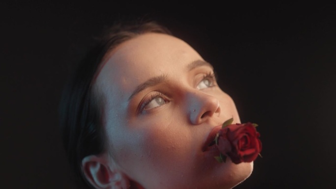 性感的女人用红色的口红和纹身黑色背景的工作室拍摄诱人的拿着一个红色的玫瑰在嘴里