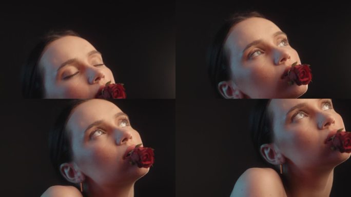 性感的女人用红色的口红和纹身黑色背景的工作室拍摄诱人的拿着一个红色的玫瑰在嘴里