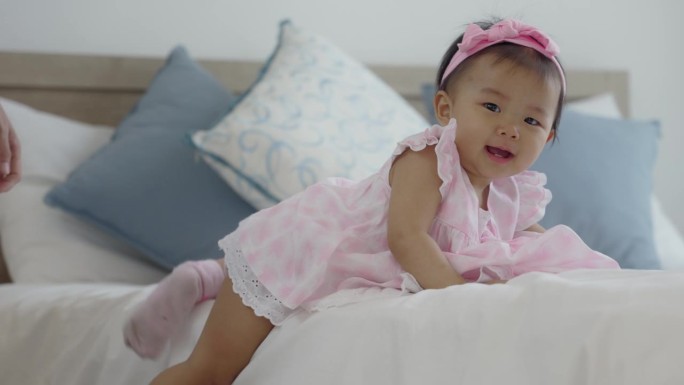 一个亚洲婴儿在妈妈的鼓励下高兴地爬下床。