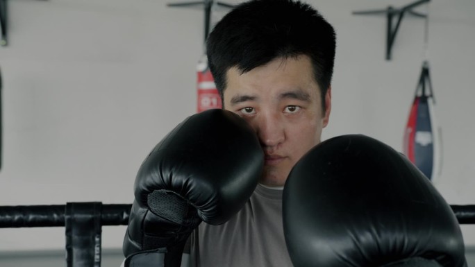 慢动作的年轻亚洲男子拳击手站在角落里戴着手套准备战斗看着镜头