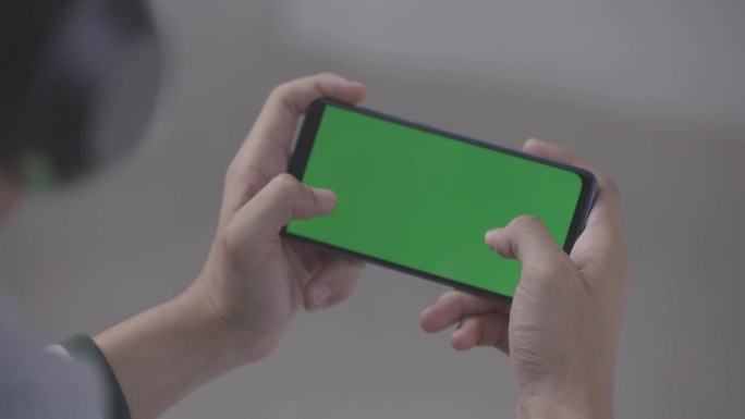 亚洲男子戴耳机玩绿屏智能手机