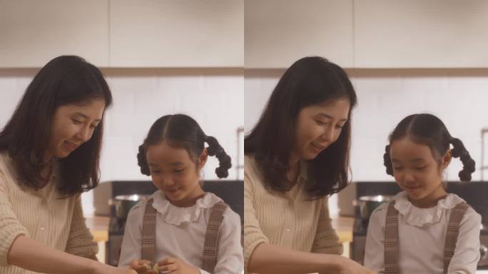 竖屏:韩国妇女和女儿在厨房一起做饭的肖像。妈妈教她的小女孩如何切蔬菜。小女孩帮妈妈准备午餐