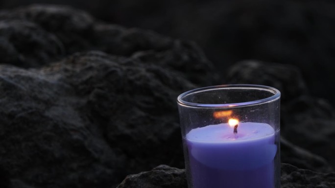 背景模糊的岩石上的Burring香氛蜡烛特写。蜡烛火焰在玻璃里发光。