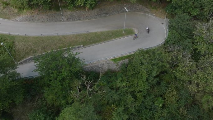 无人机拍摄的男子骑着摩托车在铺砌的道路上穿过大自然