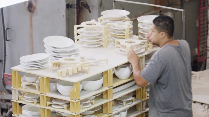 一名男子将陶瓷盘子放在陶器作坊的干燥架上