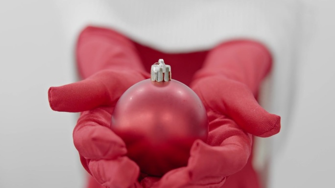 圣诞节的气氛和新年的庆祝。戴着黑色连指手套的手拿着一个红色的球。准备寒假，装饰房子，收集喜庆的圣诞树