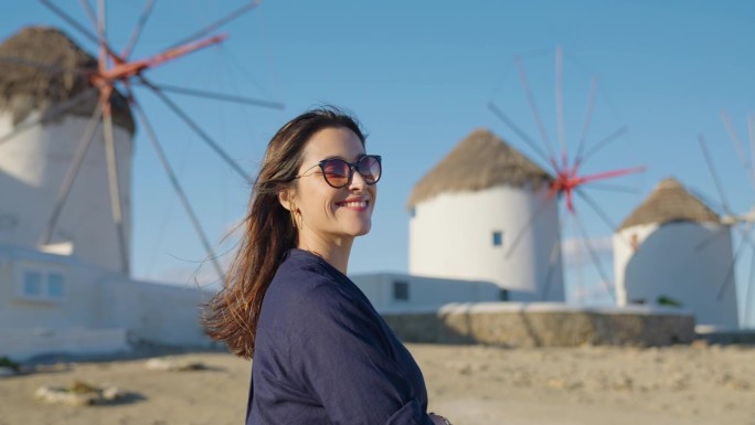 一位美丽的女游客在暑假期间欣赏着希腊米科诺斯岛著名的风车