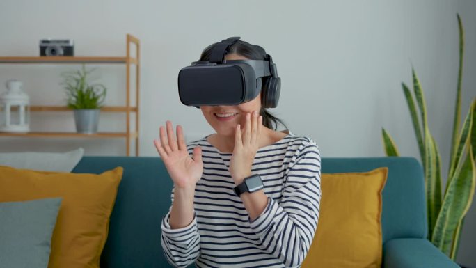 亚洲女性戴着VR头显在客厅玩电子游戏，对虚拟现实技术感到兴奋。