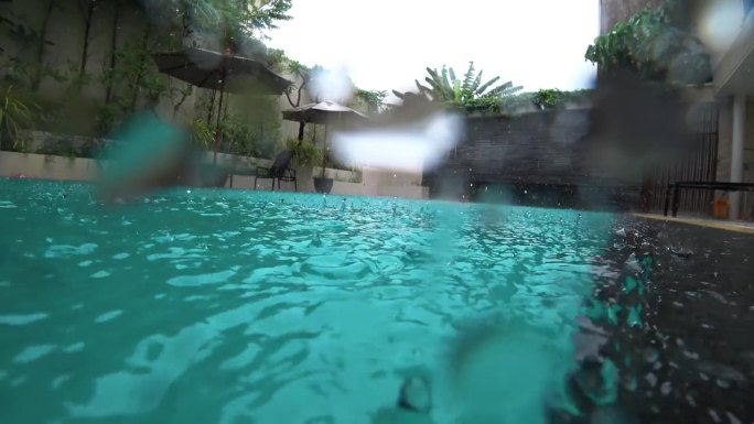 一个男人在热带雨中在旅馆的游泳池里游泳