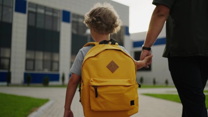 上学，小男孩背着书包，牵着爸爸的手，走在校园里，后景