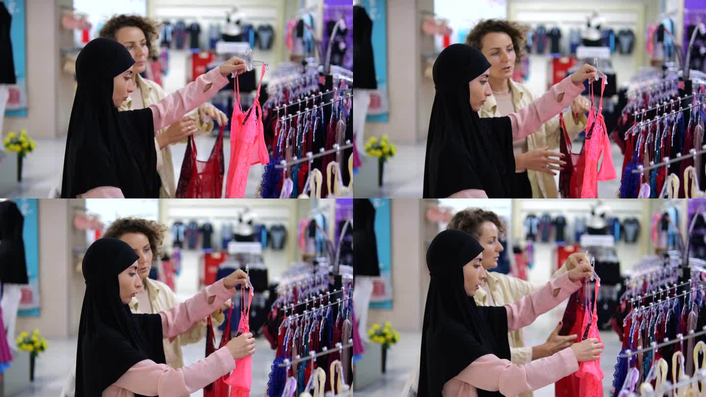 两位女性朋友在一家购物中心选购内衣。两个不同国籍的女人在一家女装店购买性感的粉色和红色内衣，她们之间