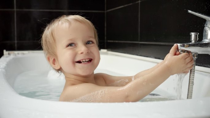 快乐微笑的小男孩玩着水龙头，在洗澡的时候玩得很开心。良好的卫生习惯对婴儿的重要性。
